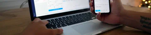 A person is looking at an open laptop and also at their cell phone
