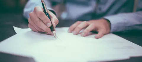 A man in business attire is using a pen to complete some paperwork